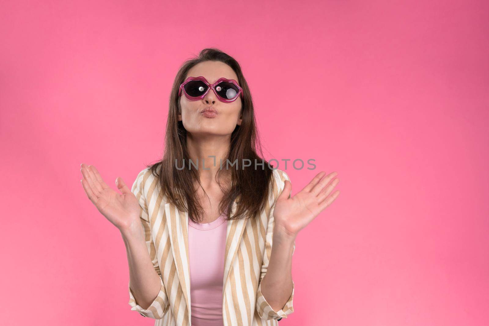 Suffering of headache or migraine young woman in sleeveless pink t-shirt holding her head with eyes shut isolated on pink background. Stressed employee woman in stripe suit. With copy space.