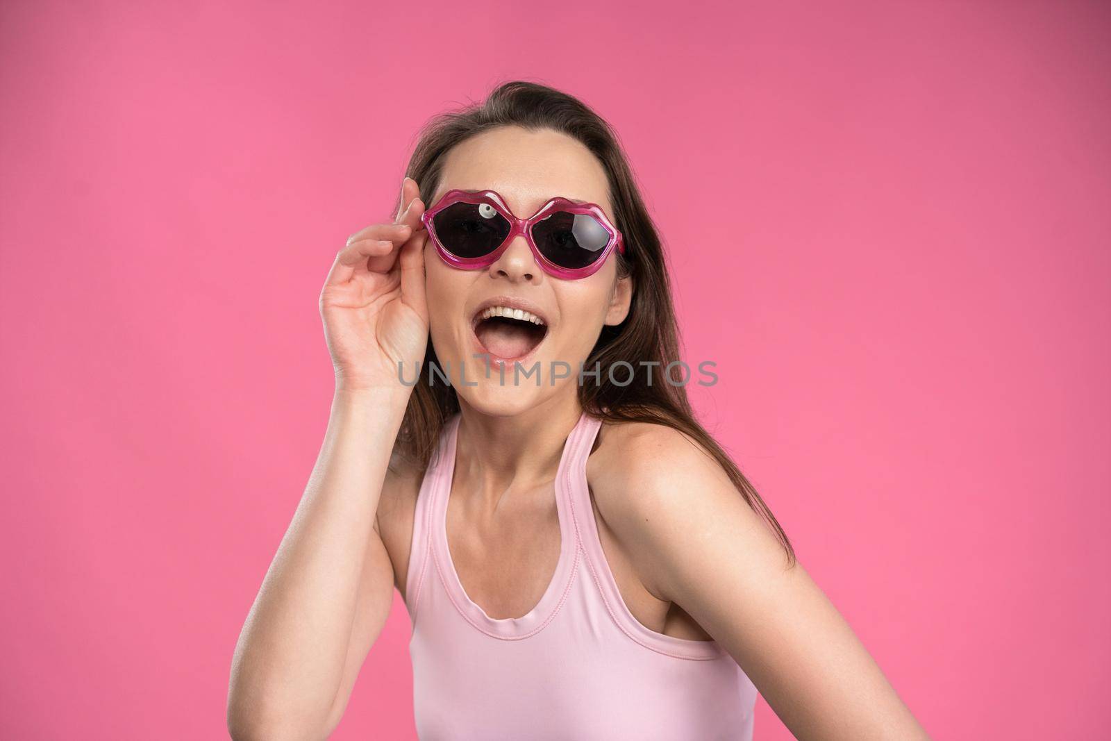 Suffering of headache or migraine young woman in sleeveless pink t-shirt holding her head with eyes shut isolated on pink background. Stressed employee woman in stripe suit. With copy space.