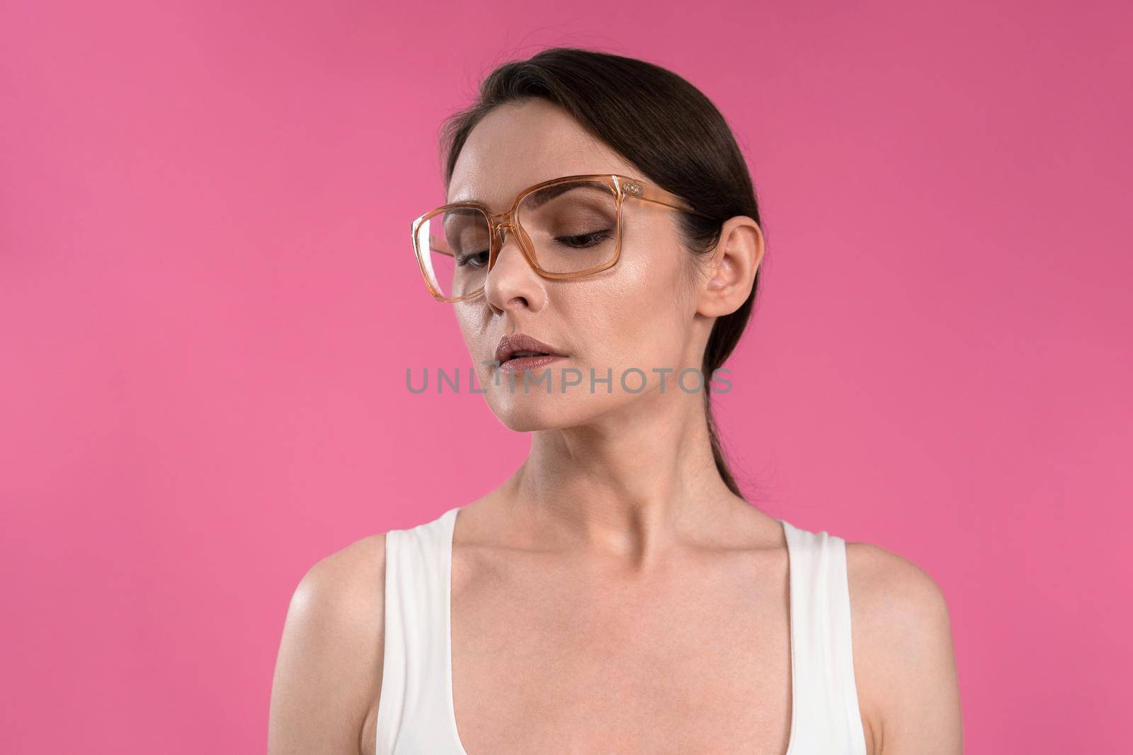 Suffering of headache or migraine young woman in sleeveless pink t-shirt holding her head with eyes shut isolated on pink background. Stressed employee woman in stripe suit. With copy space.