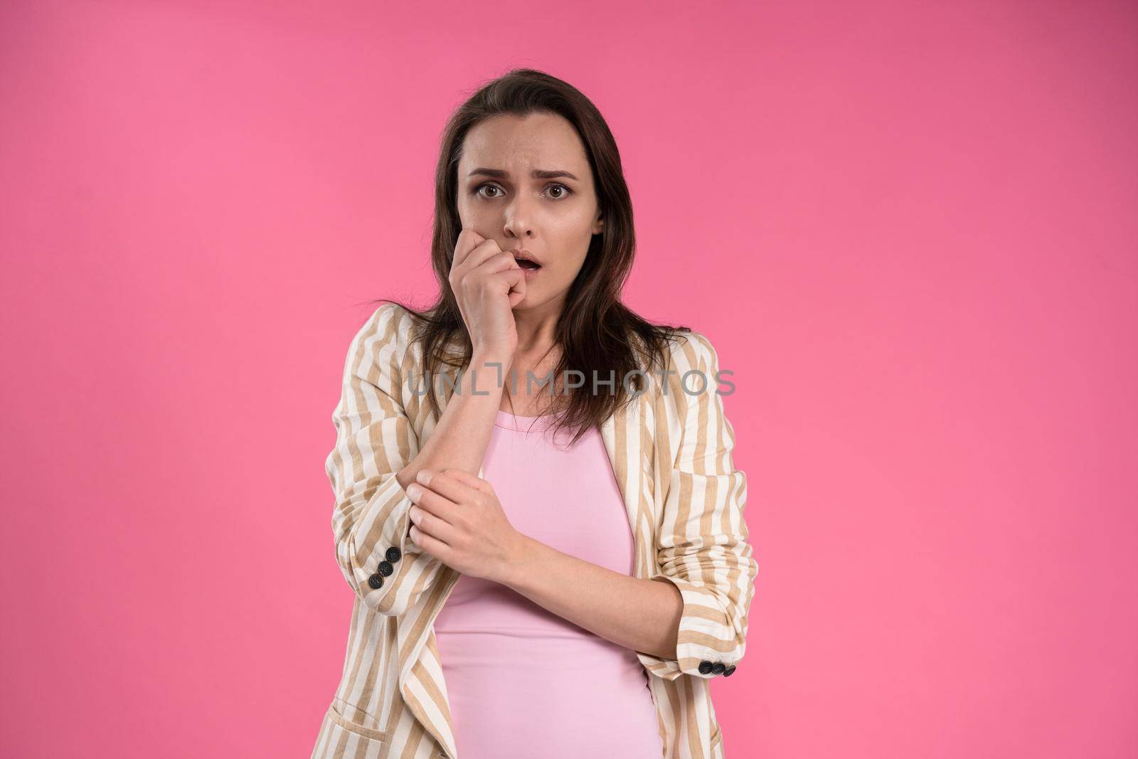 Suffering of headache or migraine young woman in sleeveless pink t-shirt holding her head with eyes shut isolated on pink background. Stressed employee woman in stripe suit. With copy space.
