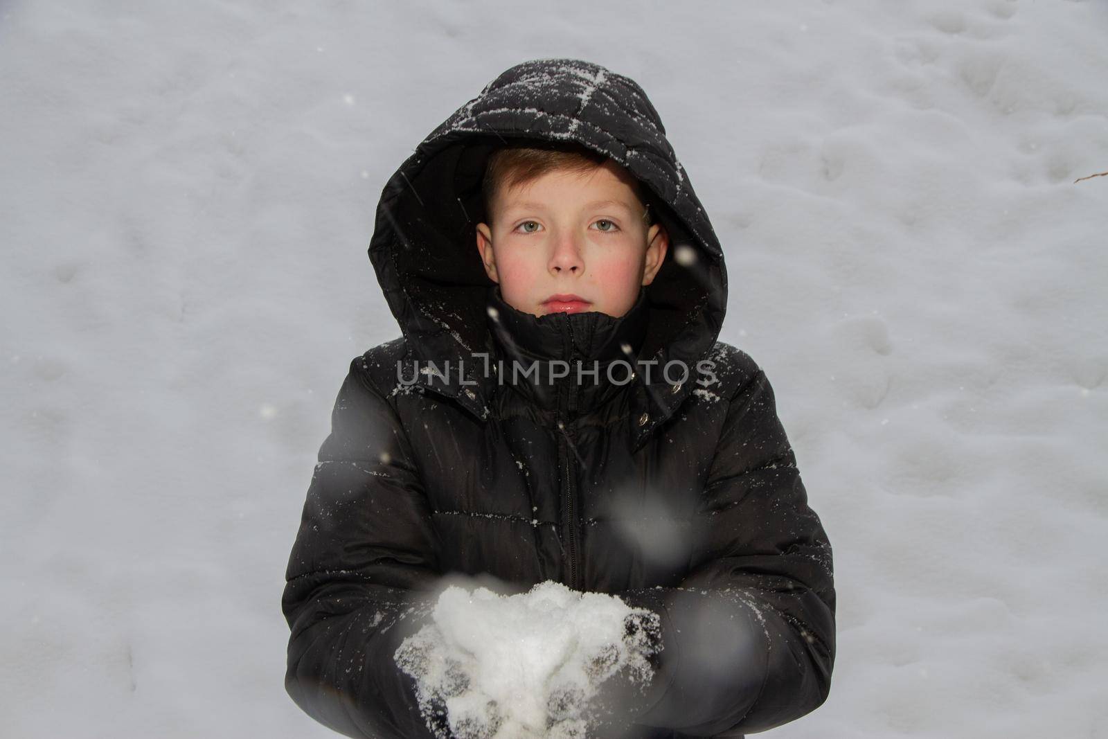 Portrait of a boy with snow in his hands on a background of snow in cloudy weather. Gloved hands hold the snow.