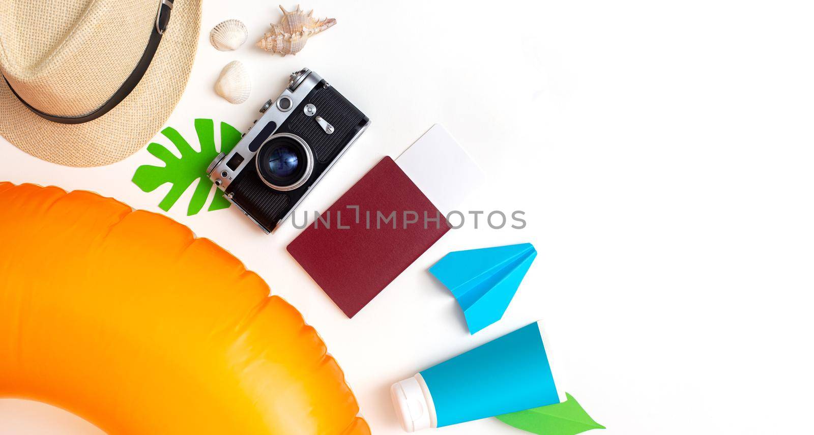 Summer travel set top view: orange swimming circle, passport, camera, straw hat, sun cream lies on white background. Copy space. Wide