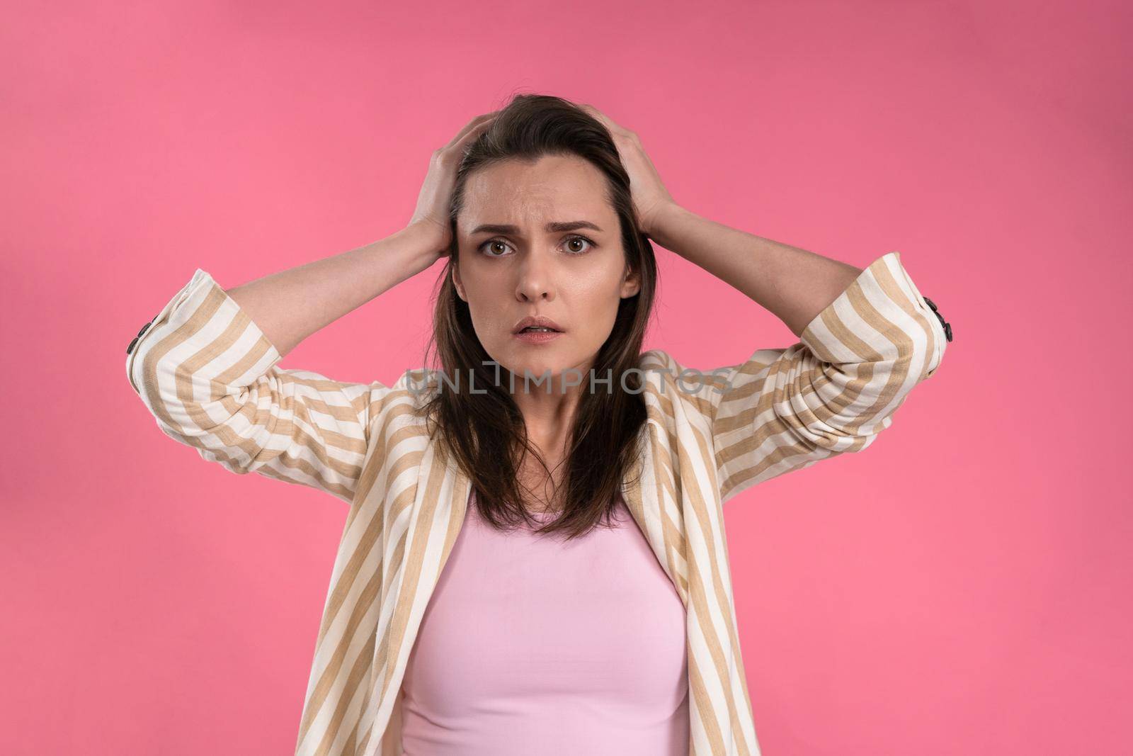 Suffering of headache or migraine young woman in sleeveless pink t-shirt holding her head with eyes shut isolated on pink background. Stressed employee woman in stripe suit. With copy space.