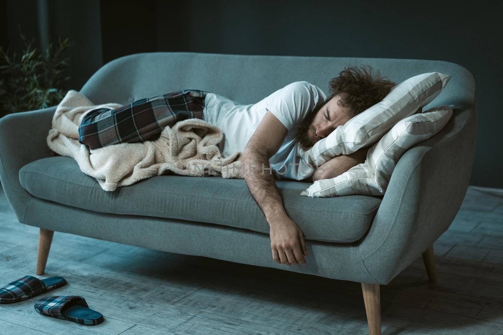 Crashed out sleeping handsome man fell asleep watching tv mid day resting on the couch or sofa enjoying weekend or quarantine days at home. Weekend relax at home.