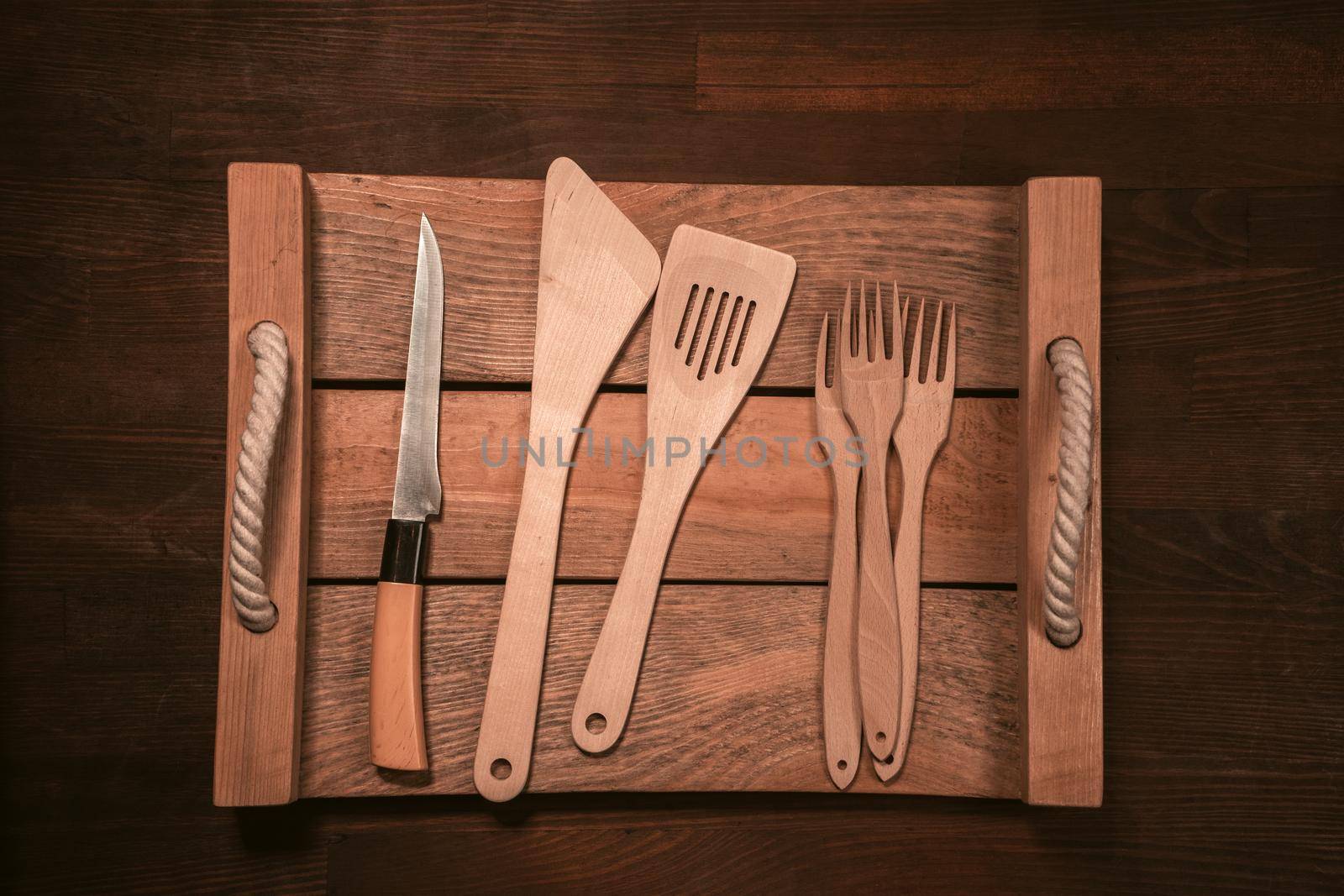 Wooden kitchen utensils laid out on wooden tray on wooden table horizontal banner. Top view.