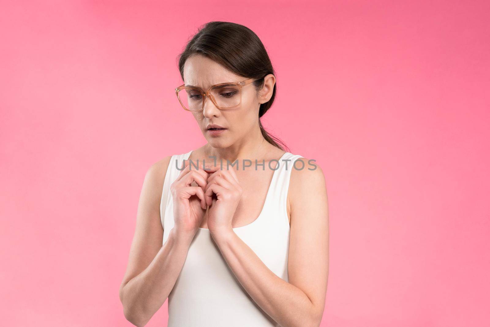 Suffering of headache or migraine young woman in sleeveless pink t-shirt holding her head with eyes shut isolated on pink background. Stressed employee woman in stripe suit. With copy space.