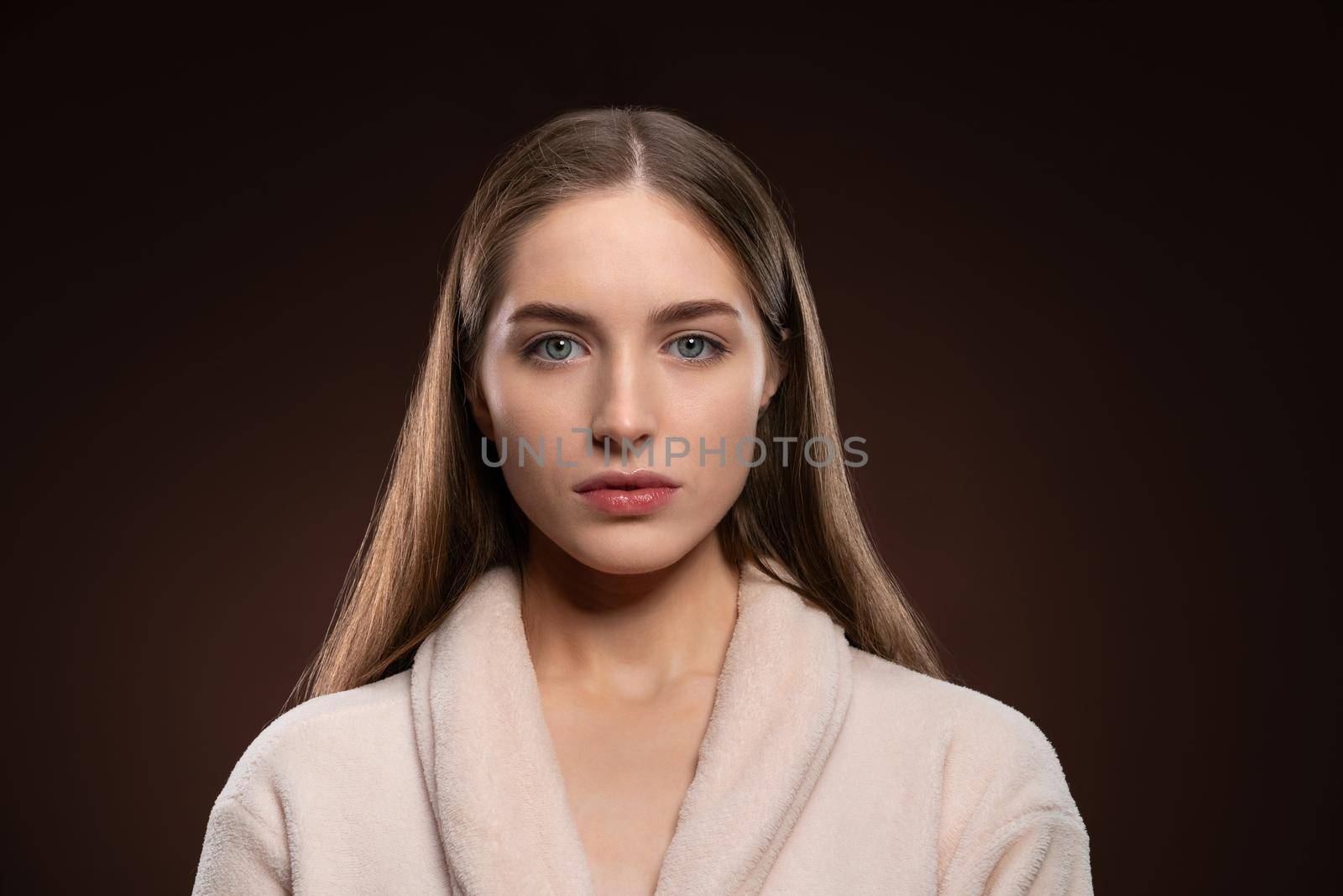 Standing in a bath robe natural beauty girl with no make up face. Healthy pure skin model posing on camera isolated on dark background. Natural make up concept. Spa and beautiful concept.