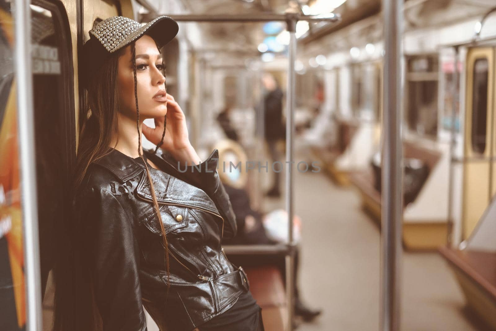 Pretty Caucasian Woman in Leather Jacket and Stylish Cap Leaning Back against the Underground Train Door. Beautiful Face. Close-up Portrait. Toned picture. High quality photo