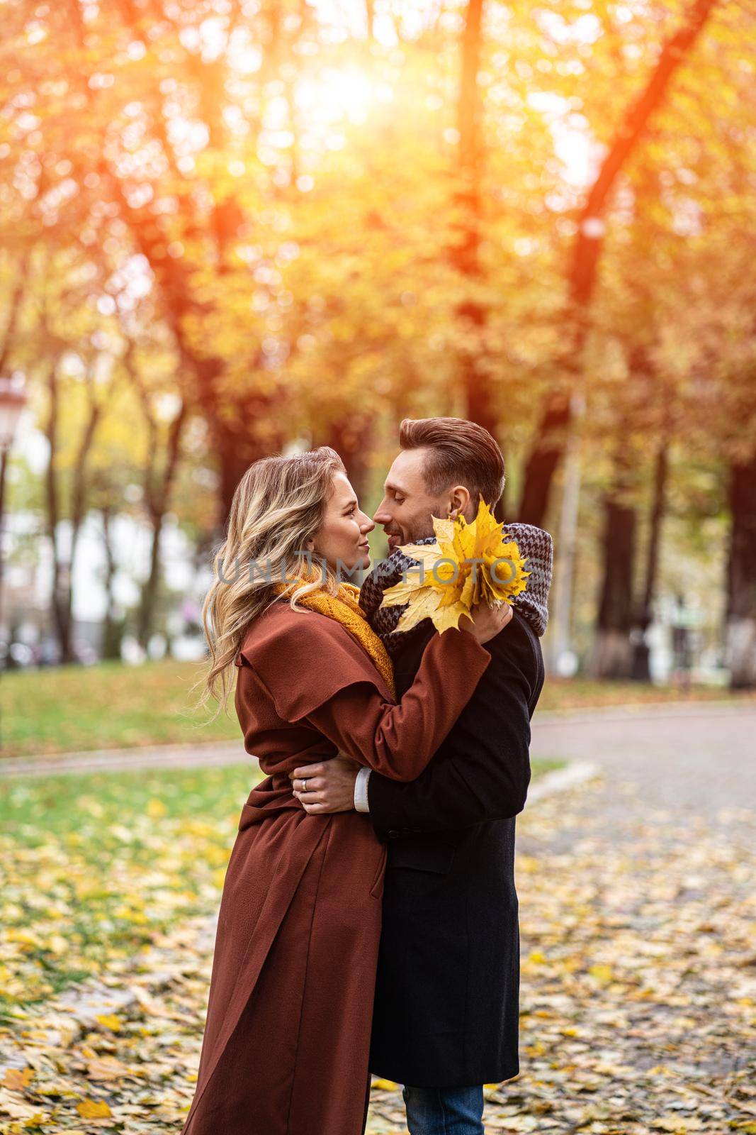 Husband and a wife hugged smile looking at each other in the autumn park. Half-length portrait of a kissing young couple. Outdoor shot of a young couple in love in a autumn park.