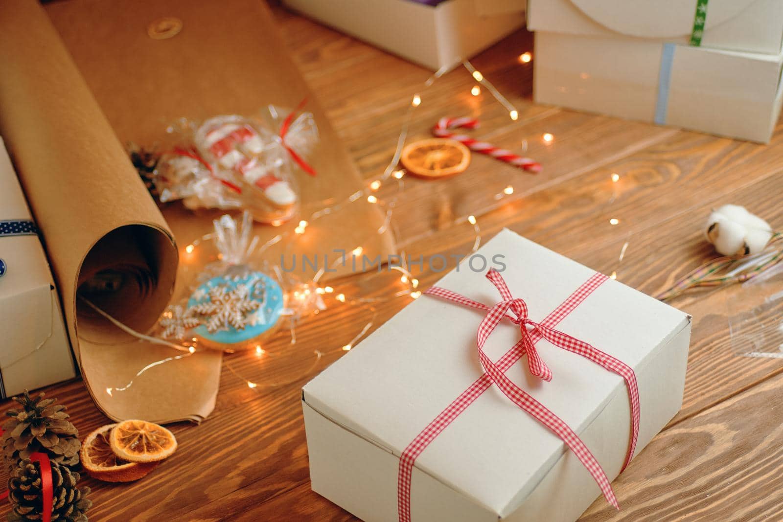 Christmas gift with red ribbon, gingerbread, sweets, craft wrapping paper, pine cone and garlands on wooden table. Festive mood and holiday decorations. Surprise for New Year.