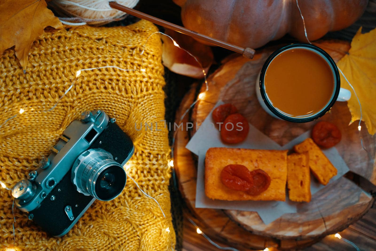 Top view of the festive composition. The concept of Thanksgiving. Cocoa, carrot pie, dried apricots on a wooden tray. Knit sweater, a vintage camera, round pumpkin, garland and autumn yellow leaves.