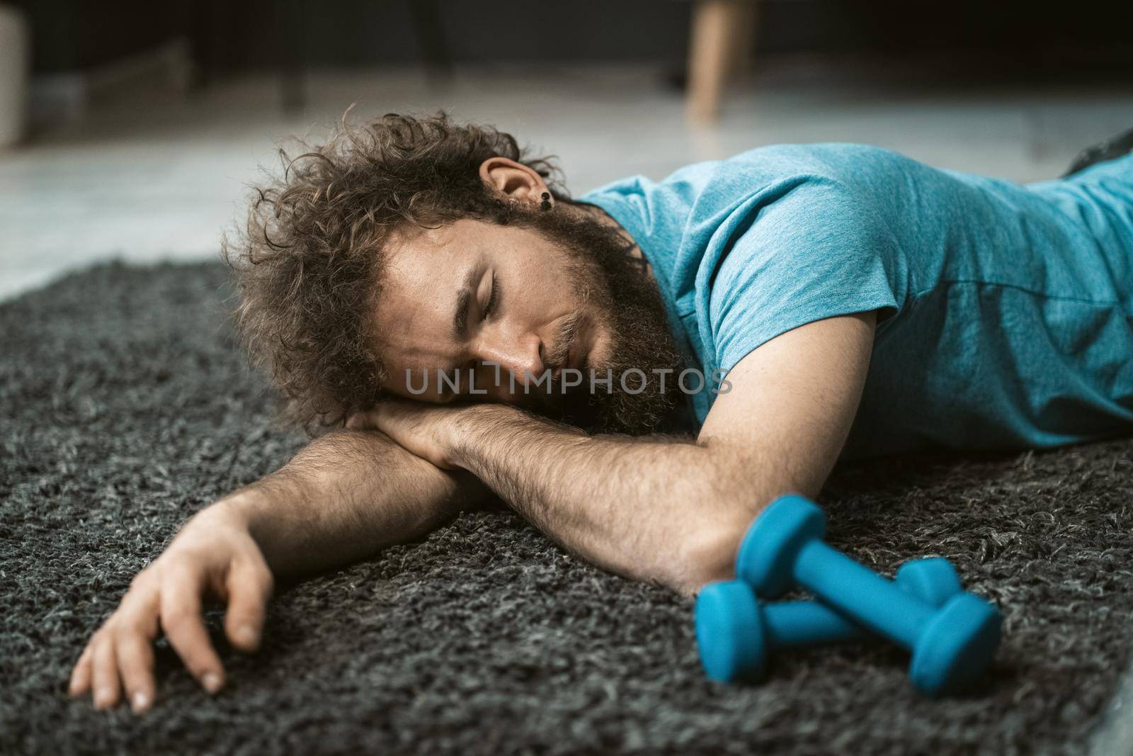 Exhausted of home exercise man laying on the carpet and resting. Funny disheveled hair man doing exercise at home. Tired young man doing exercises at home on quarantine. Concept of healthy life.