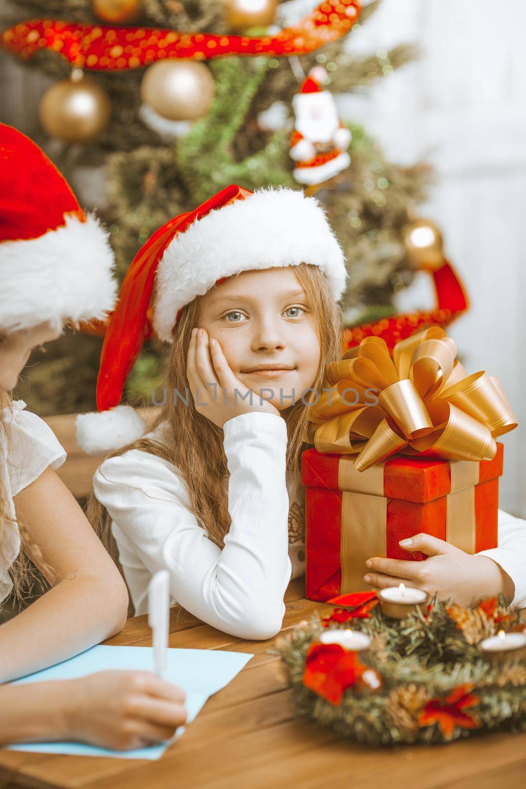 Little Sisters Girls in Christmas Hats Write a Letter to Santa Claus and Enjoy Christmas Eve. High quality photo
