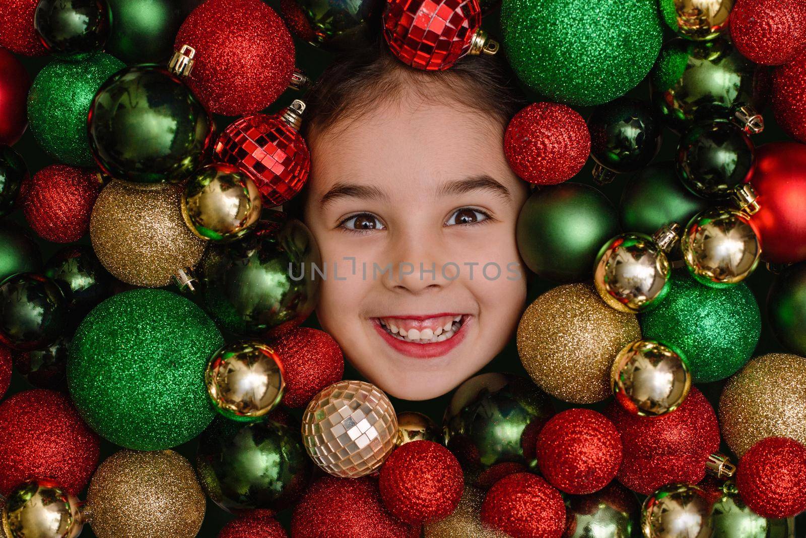 Cheerful portrait of a little girl in red, green and gold Christmas balls.