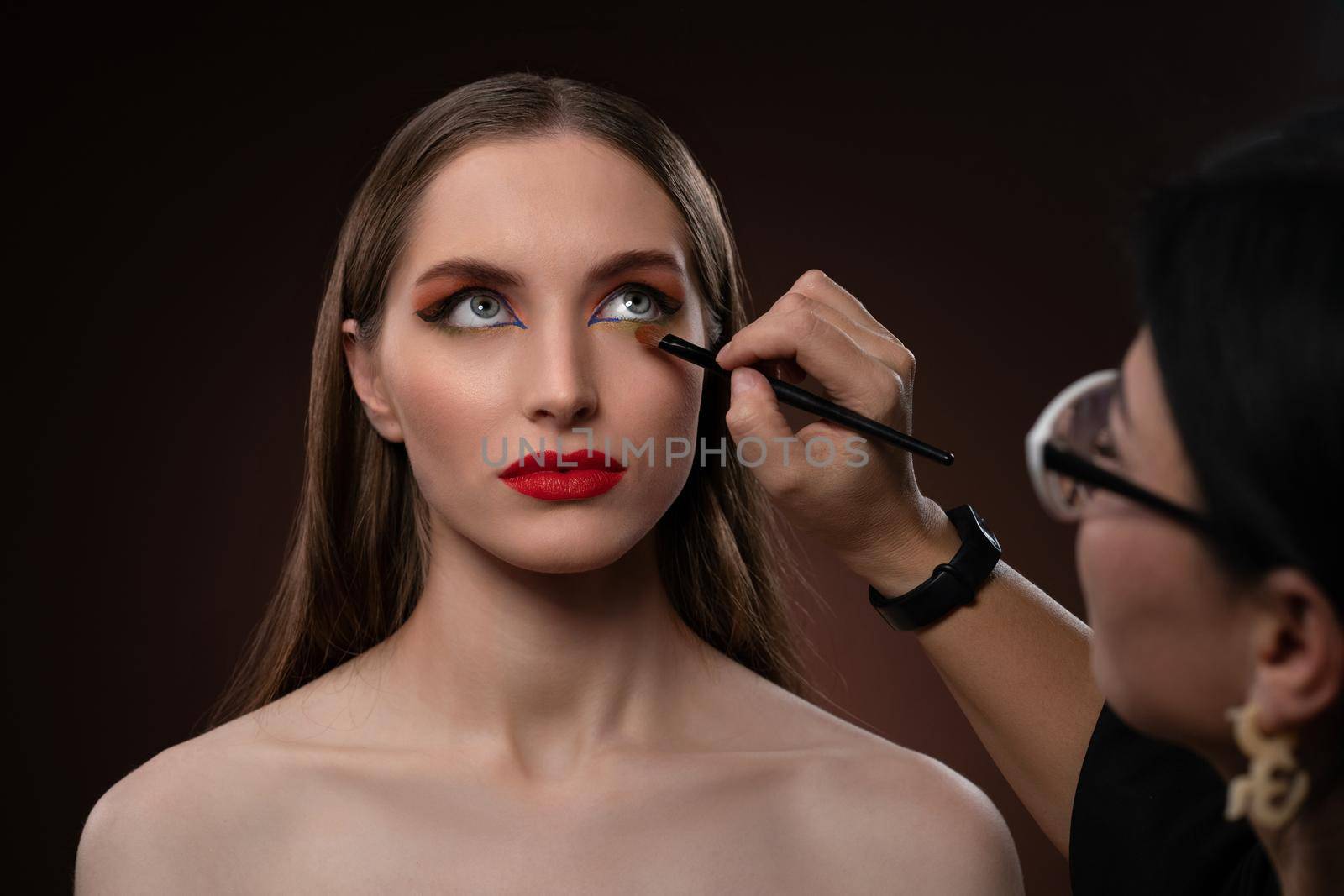 Close up on model. Beautiful model at MUAH artist. Beauty makeup artist working on a fashion model face isolated on black background. Make-up artist, applying eye shadow to the model.