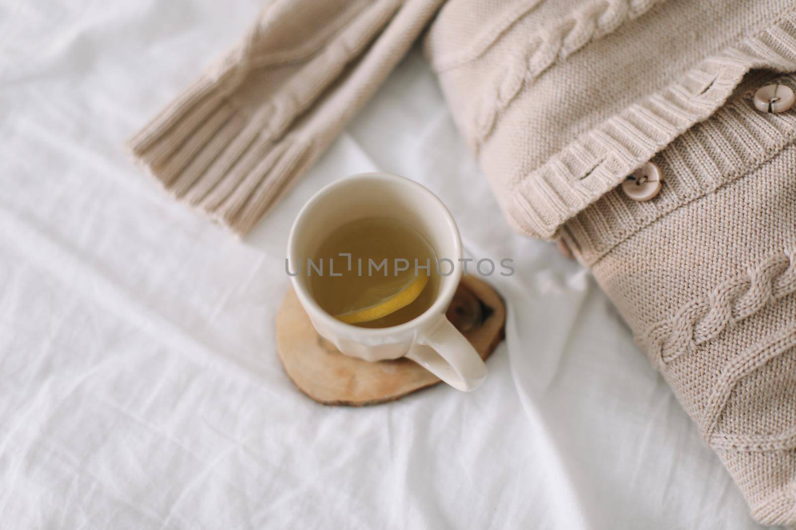 Knitted beige sweater and cup of tea on messy bed background. Winter and spring fashion concept. Top view flat lay. by paralisart