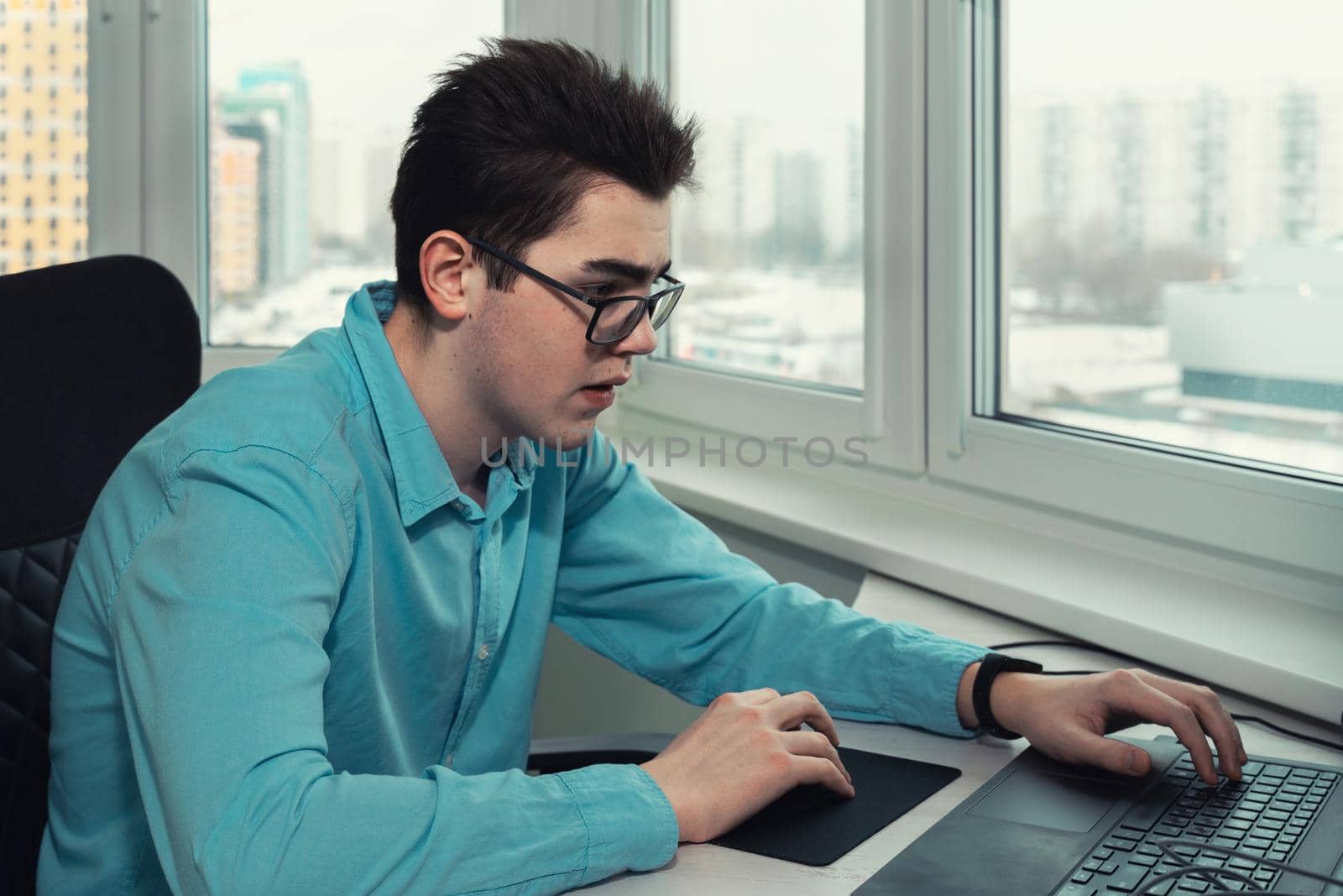 young employee with glasses looking at laptop screen and typing.