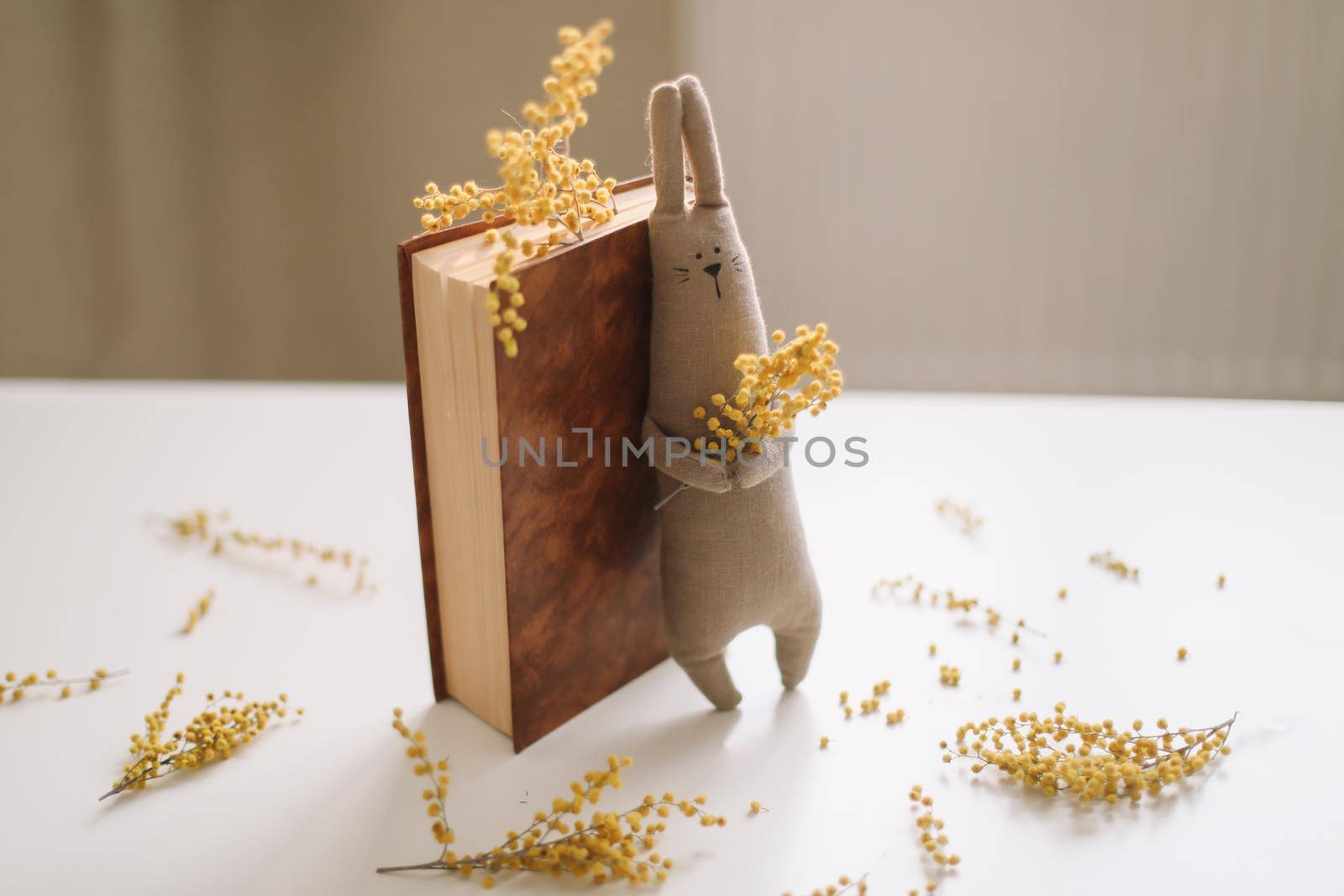 A book and a funny handmade bunny rabbit toy with mimosa flowers. Easter gift concept. 