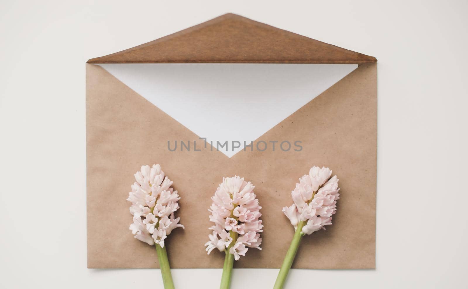 Craft paper envelop with white card and pink flowers on white background. 