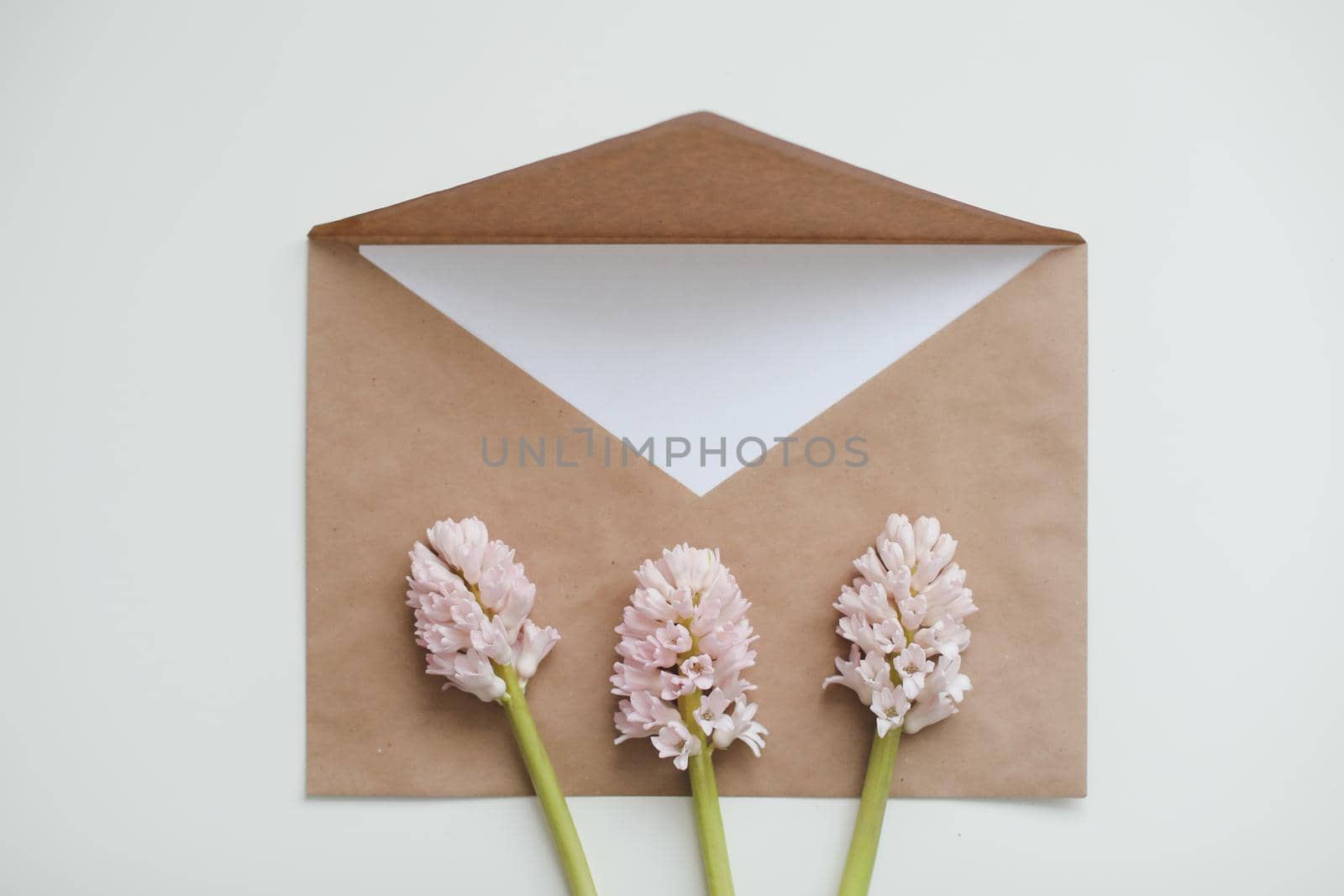 Craft paper envelop with white card and pink hyacinth flowers on white background. Top view, flat lay, copy space. Holiday festive minimal background 