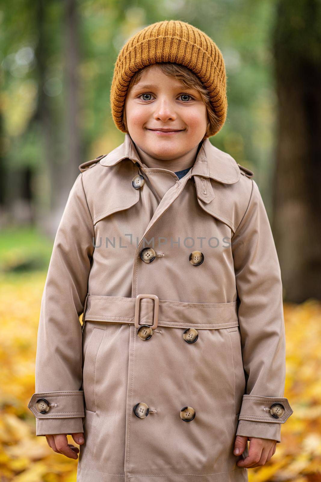 A cute little boy in an autumn coat and a hat is standing on the autumn street and smiling cutely at the camera. Tinted image.