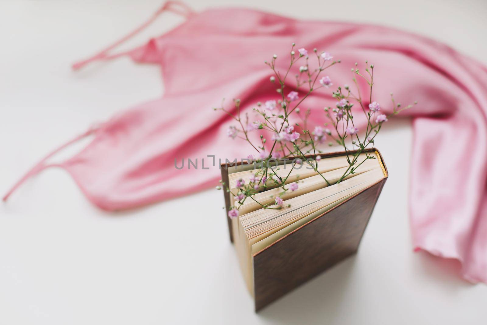 Flat lay composition with elegant pink dress and a book with flowers on beige background.