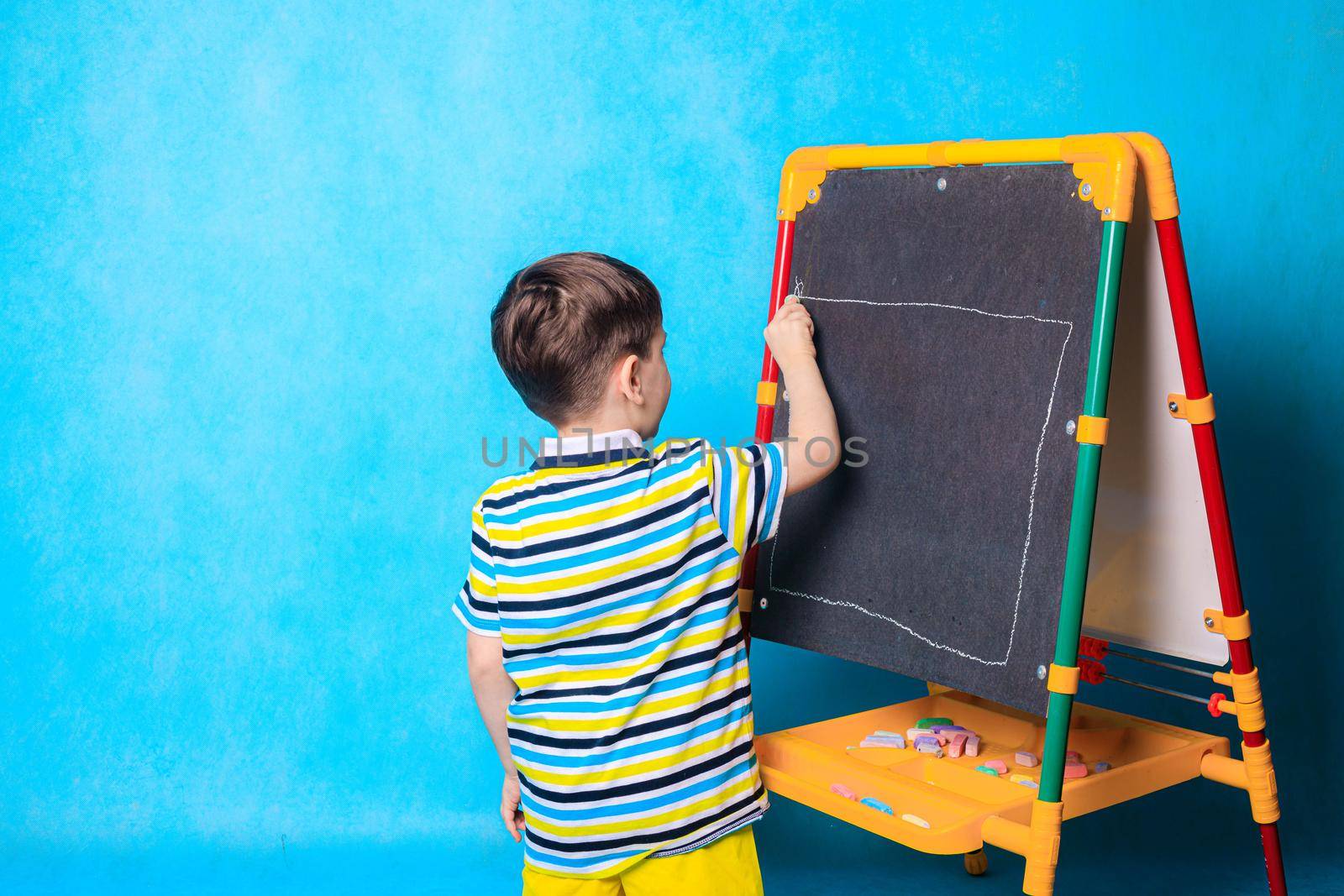 The boy draws on the blackboard with a chalk . A boy on a blue background. An article about children's leisure. Drawing board