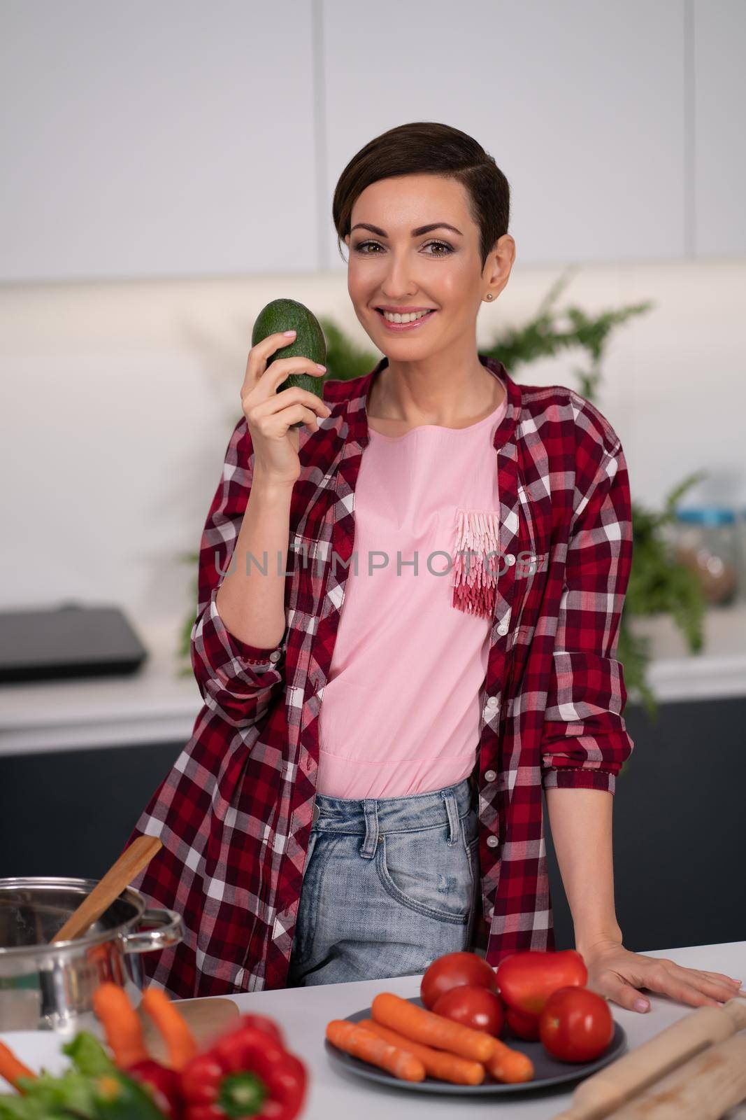 Fresh avocado in the hand of a pretty housewife with a short hairstyle prepares food in the kitchen. Healthy food at home. Healthy food leaving - vegan concept.