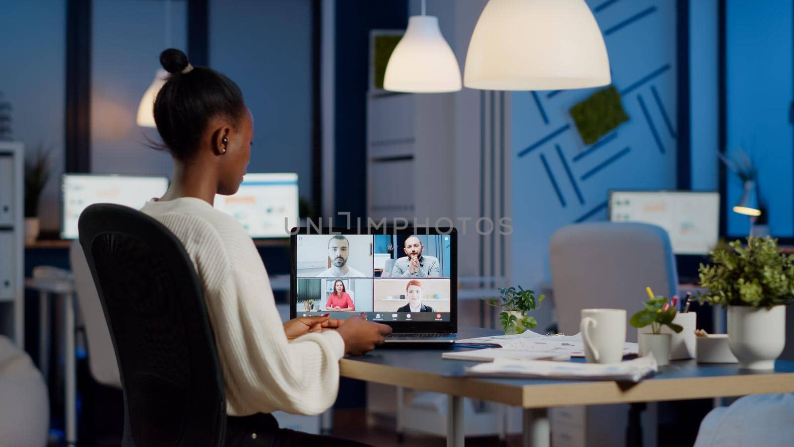 African employee working overtime from business office late at night discussing with partners online using webcam. Diverse team talking during corporate meeting using technology network wireless