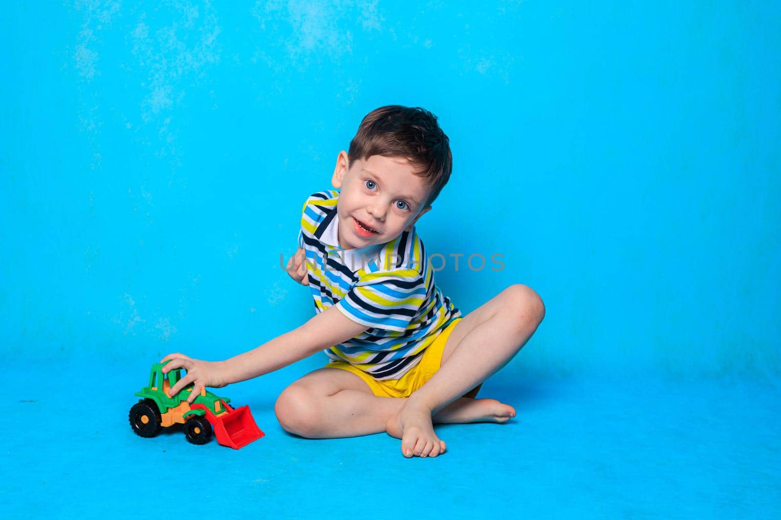 A boy is playing a typewriter on a blue background . An article about children's leisure. Children's games. Children's cars. Copy Space