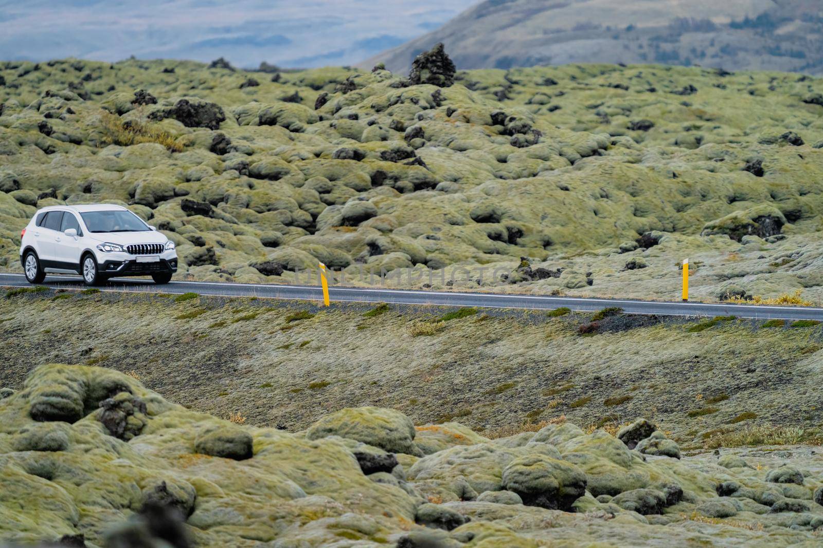 White car driving through lava fields covered by moss in Iceland