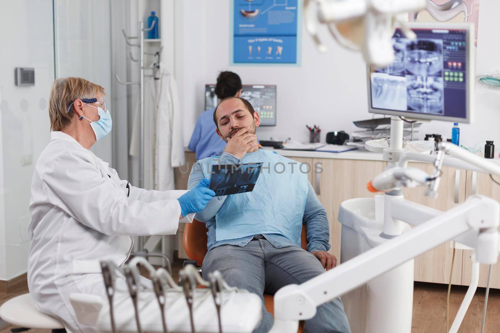 Senior dentist woman with face mask explaining teeth radiography by DCStudio