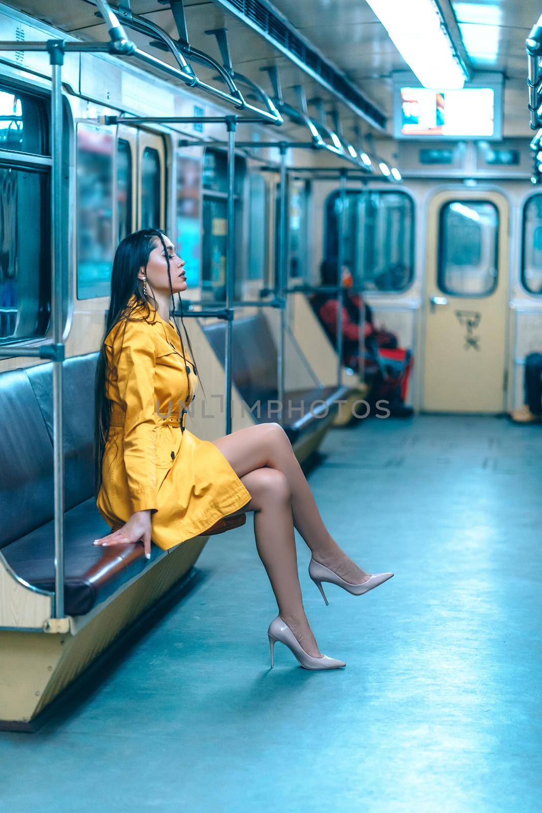 Charming Lady in a Cute Sexy Yellow Dress with Delightful Slender Legs Sitting Inside the Empty Underground Train. Full Size Profile of Nice Woman in Yellow Coat in the Train. Close-up . High quality photo