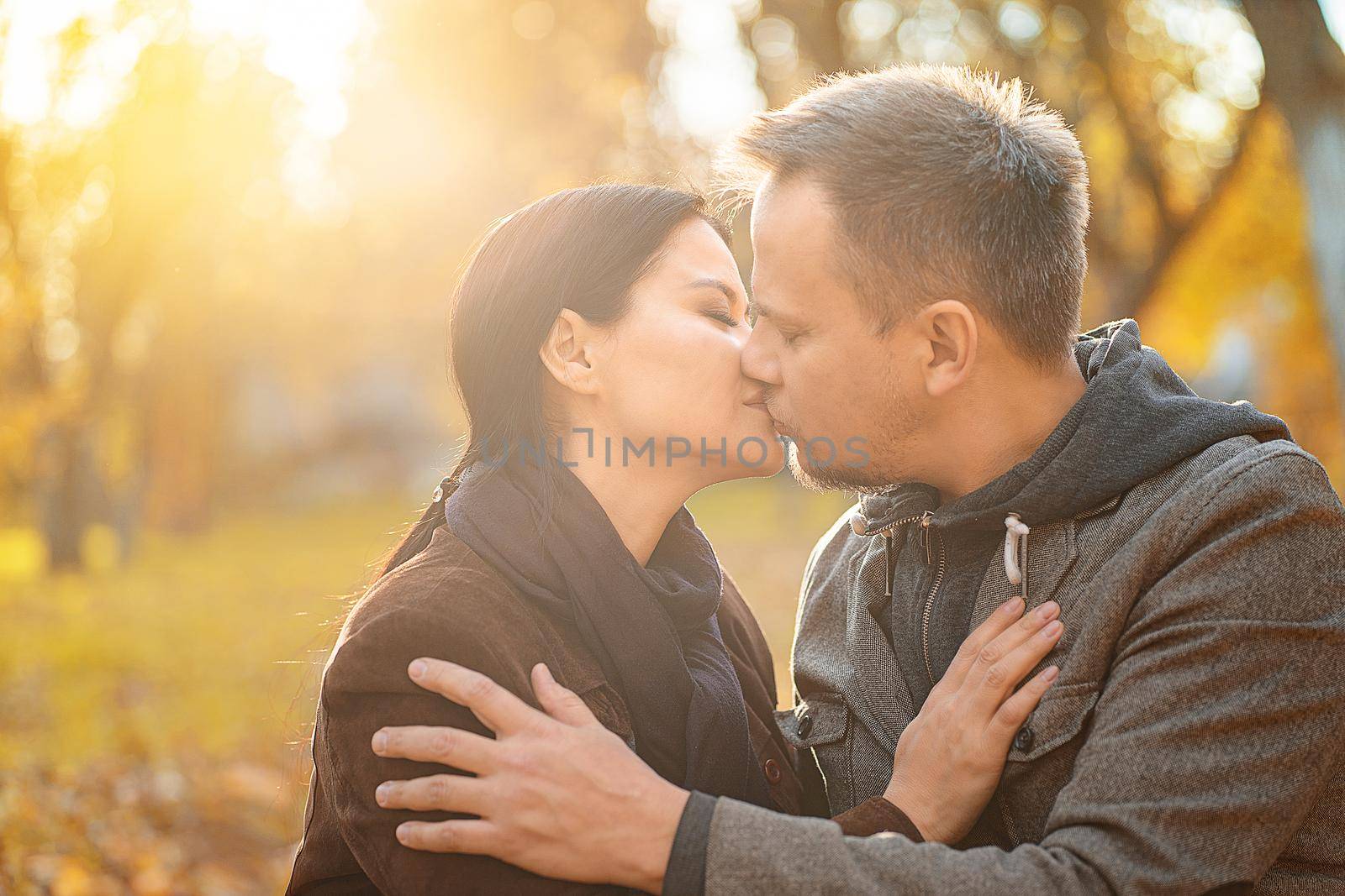 Couple In Love Kissing in the Sun Shining. Husband and His Wife Kissing on a Sunny Meadow in the Autumn Forest. Close-up. Fall Background by LipikStockMedia