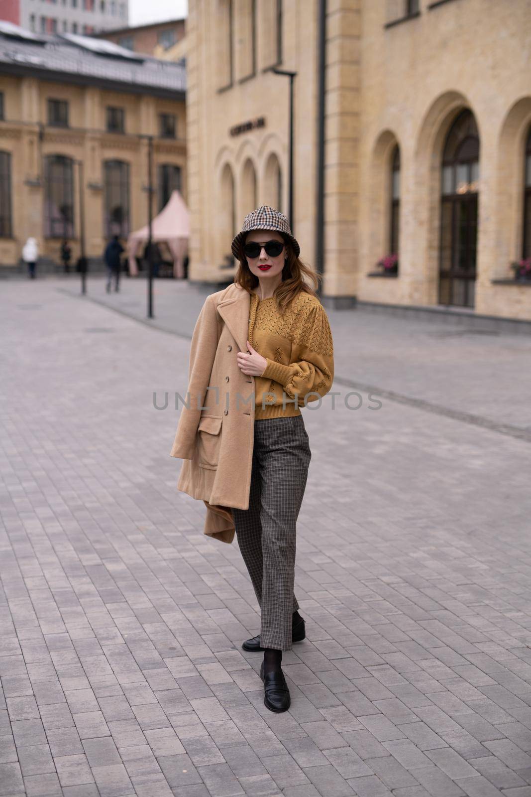 Charming model girl in an autumn beige coat and sunglasses, plaid panama hat standing with face turned holding coat on her shoulders. Retro toned photo by LipikStockMedia