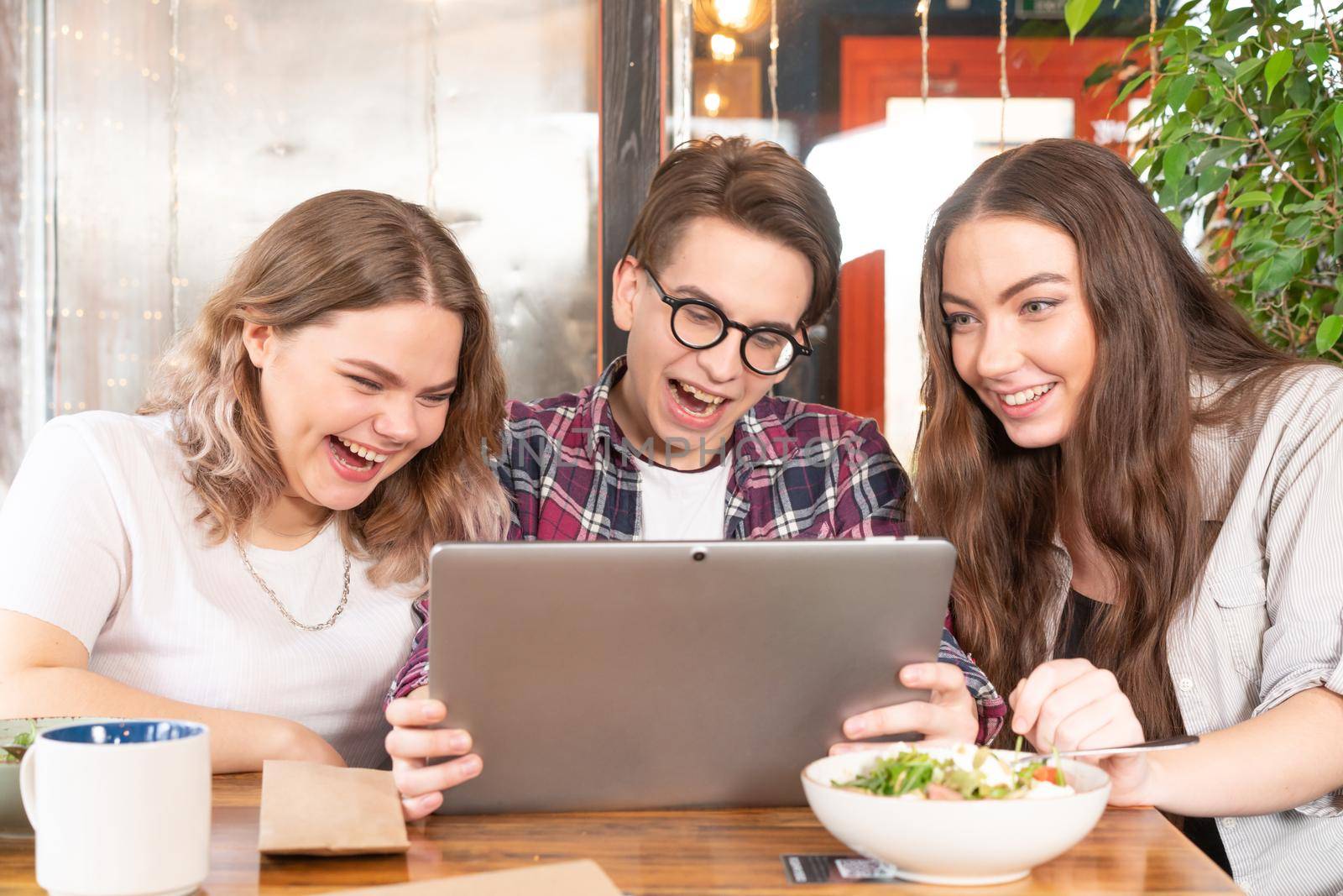 Friends having fun at cafe looking at tablet pc watching fun videos or having video call or social media. Three friends at cafe or street food restaurant spend time together. street food concept.