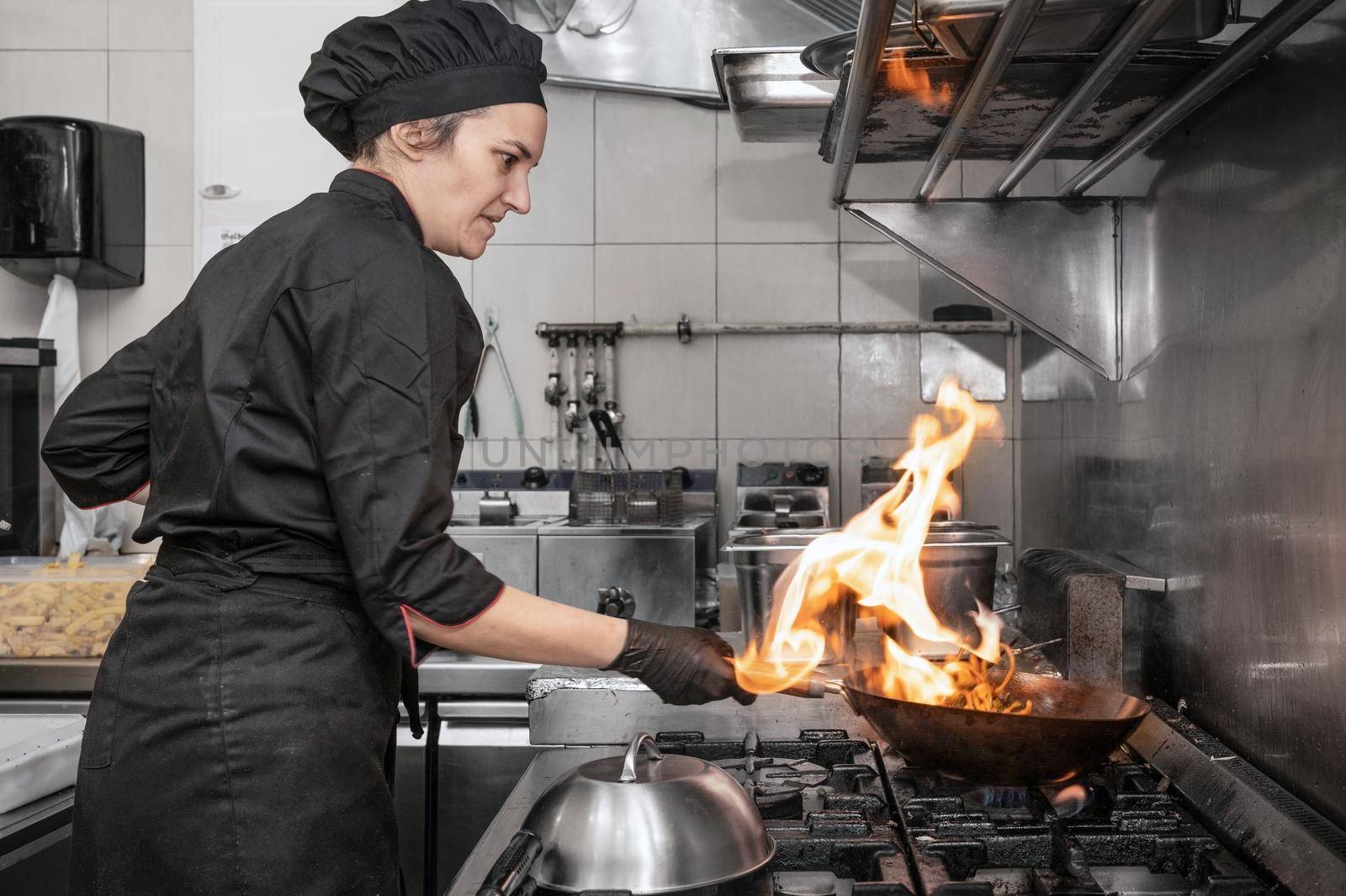 Woman Chef Cooking wok in the Kitchen. Cooking flaming wok with vegetables in the commercial kitchen. High quality photography.