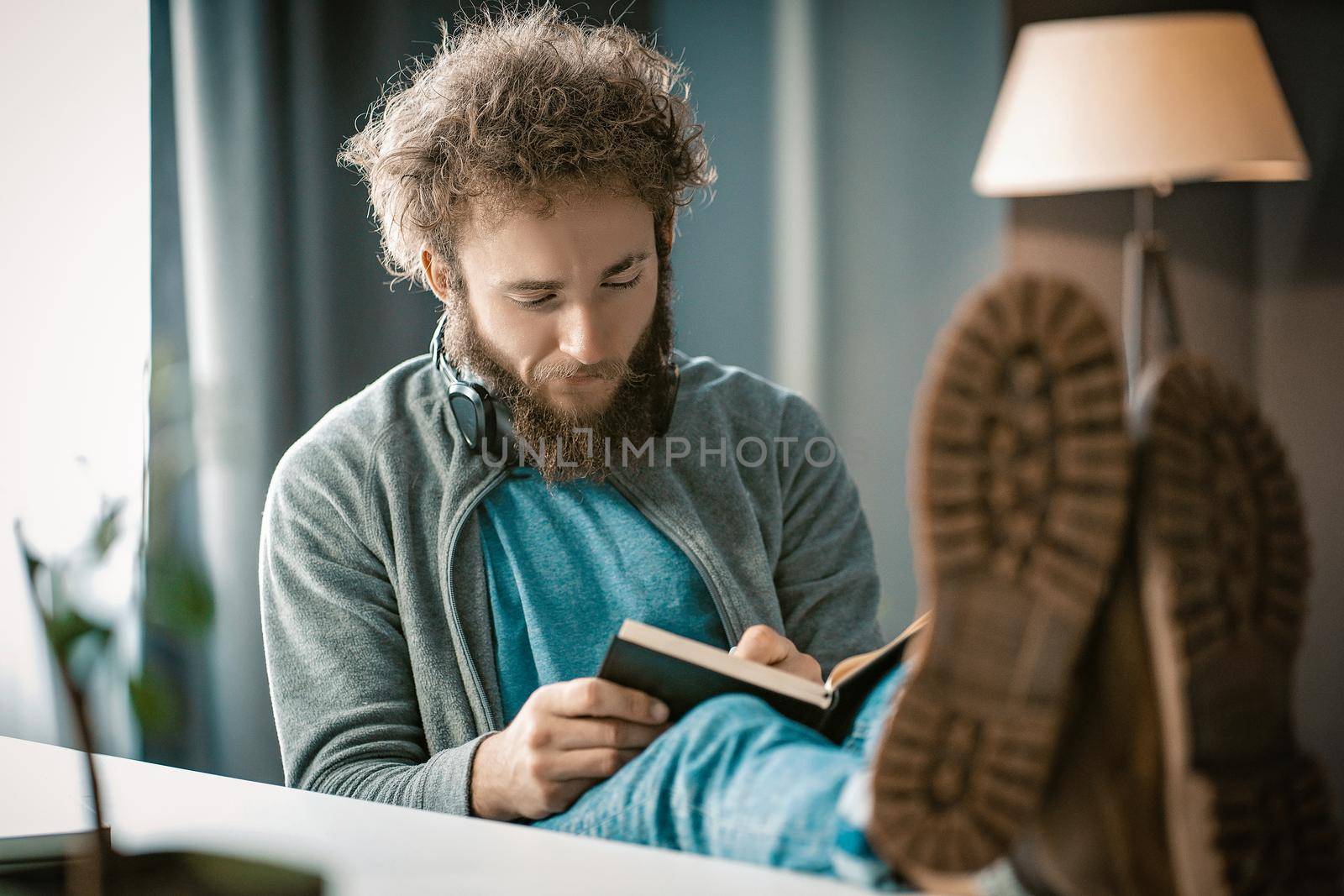 Curly-haired Guy Writes his Thoughts in a Diary. A Man Taking Notes in a Diary. Feet on the Table. Close-up. High quality photo
