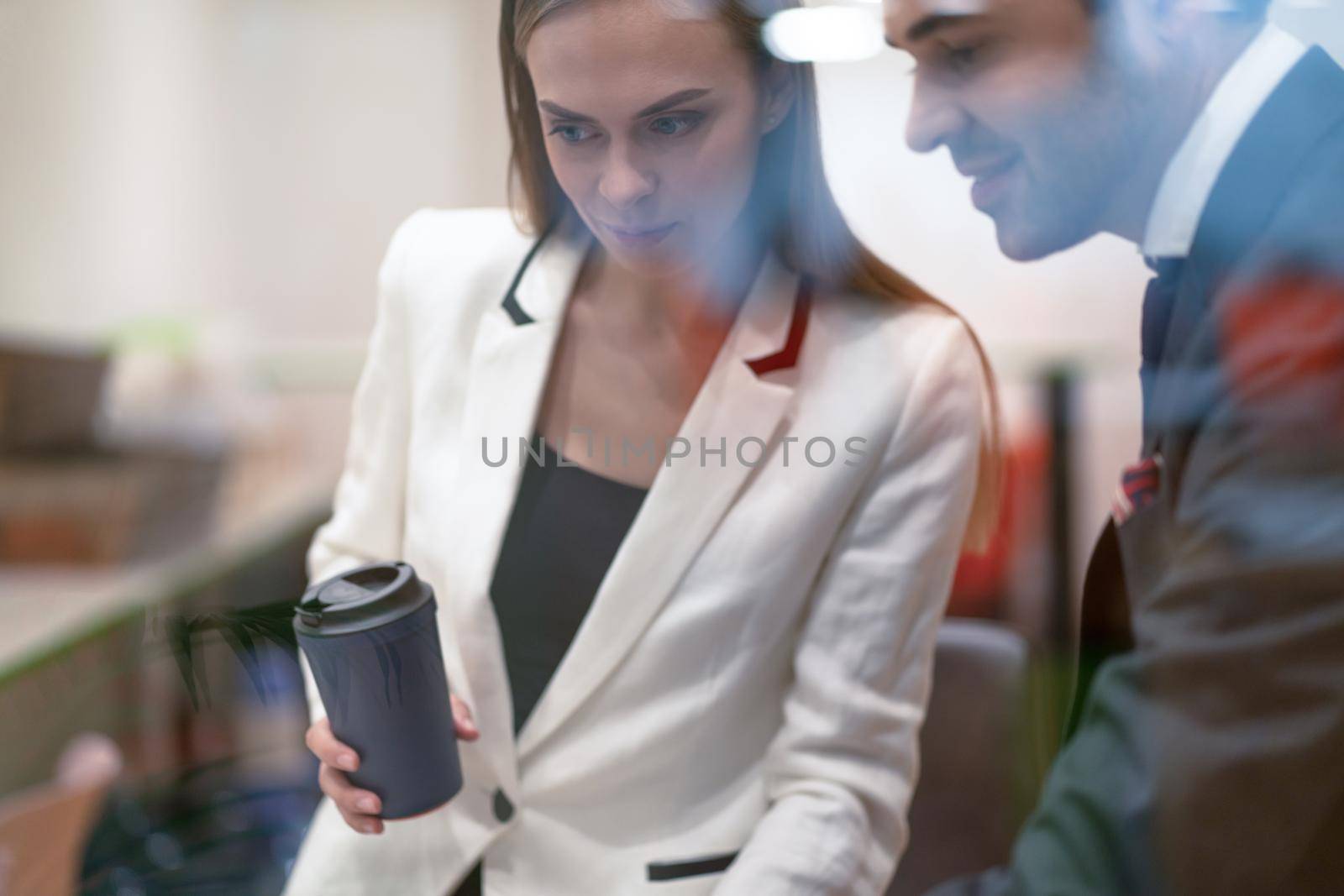 Two colleagues discuss project updates while having a coffee break. Young business people in the suits with coffee in hands looking down standing behind the glass.