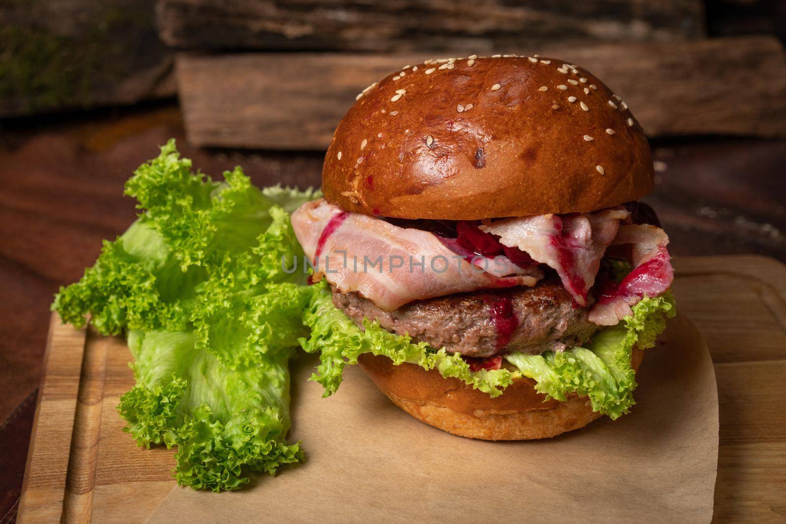 Served fresh craft beef burger with fried slices of bacon and cherry sauce, fresh lettuce laying next to it. Restaurant concept. Street food concept.