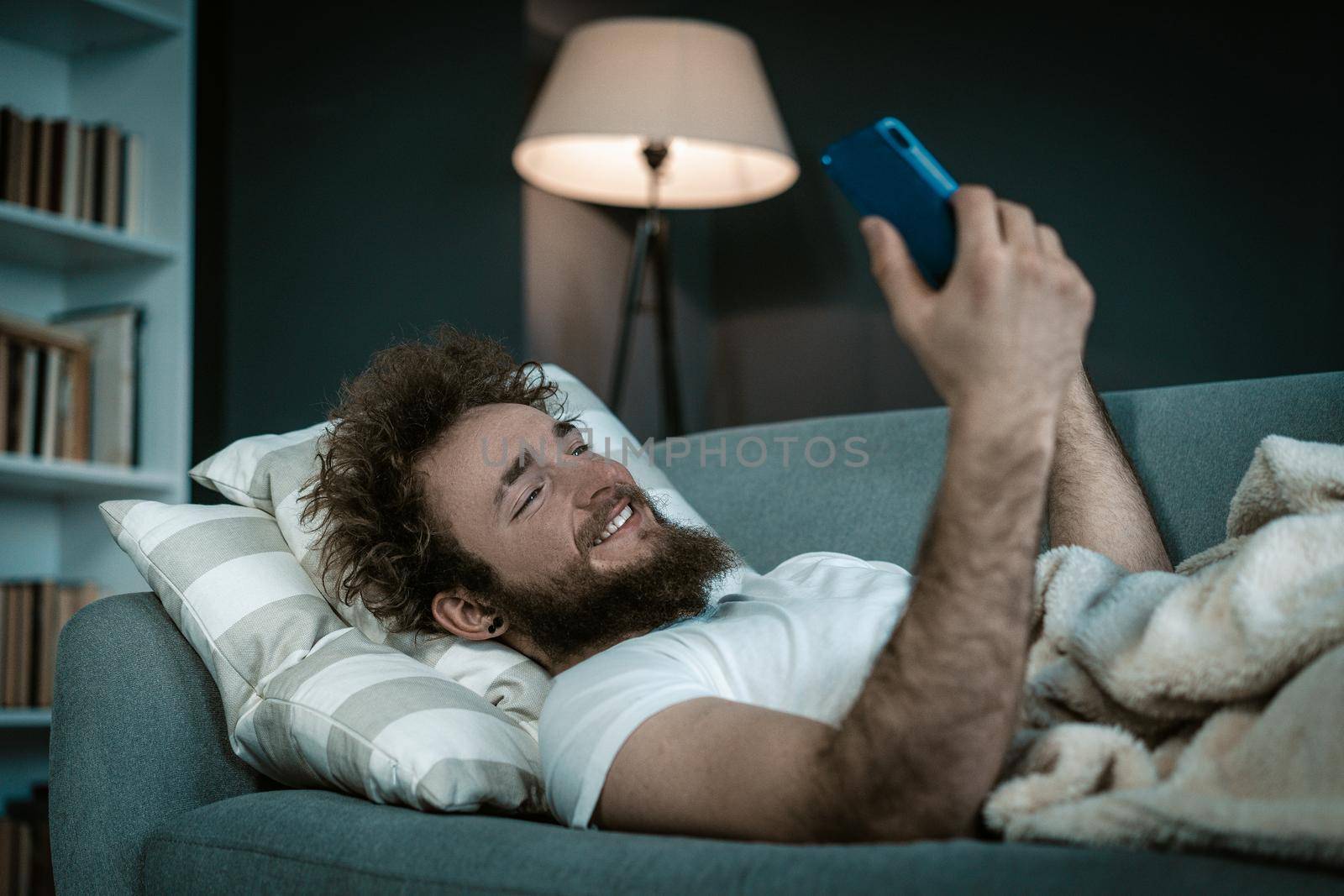Shapely Guy Watches his Favorite Serials on his phone before going to sleep. He watches serials the whole night in his bed. Close-up. High quality photo