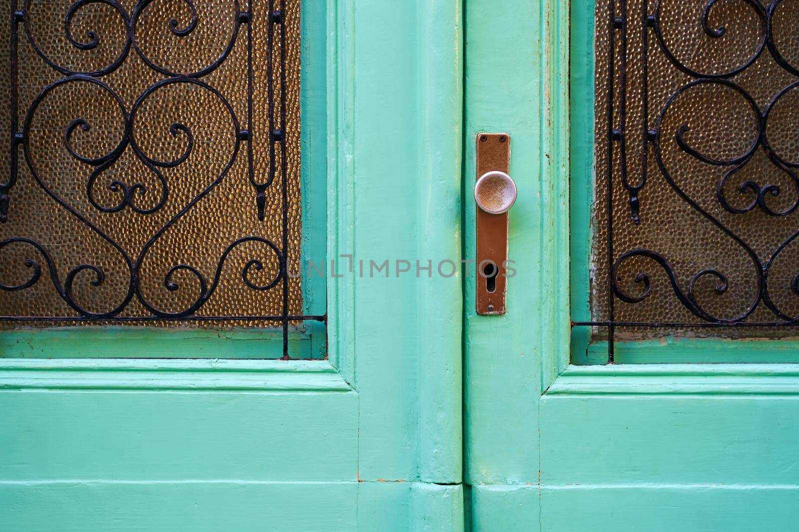 Old turquoise Mediterranean style vintage door with handle, keyhole and glass parts with forged figured lattices