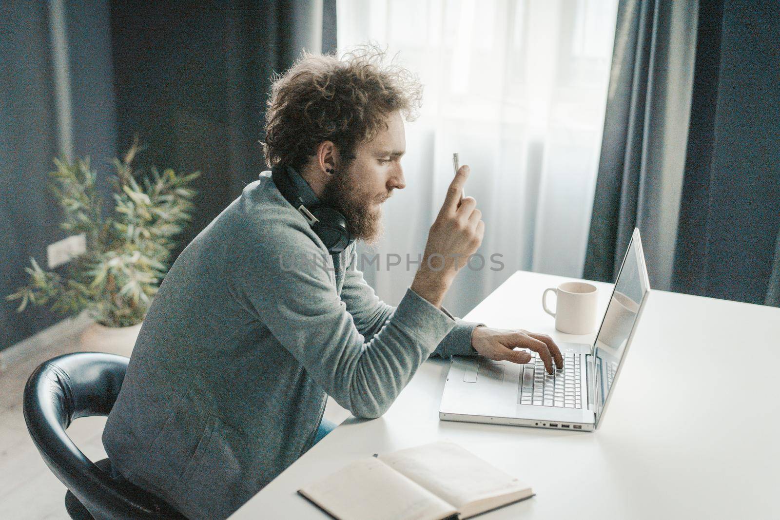 Young Businessman Analyzes New Online Business Strategies During the Quarantine Period. Young Man Sitting at the Table With a Cup of Coffee and Typing Text on His Laptop. Close-up. High quality photo