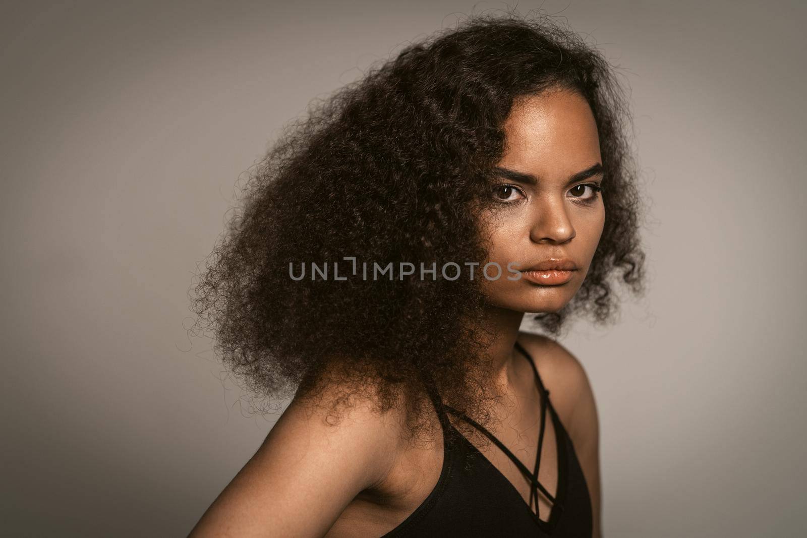Contempt or hate African American girl with afro hair standing in black bare shoulder top isolated on grey background. Human emotions, facial expression concept.