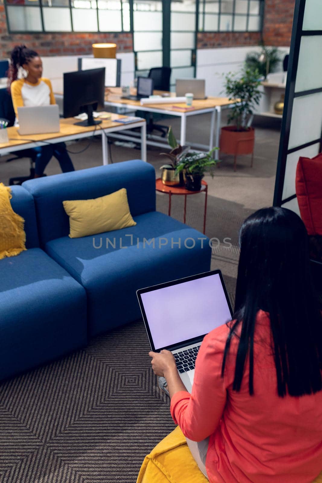 Biracial young businesswoman using laptop and african american young female colleague using desktop. unaltered, creative business, copy space, modern office and wireless technology concept.