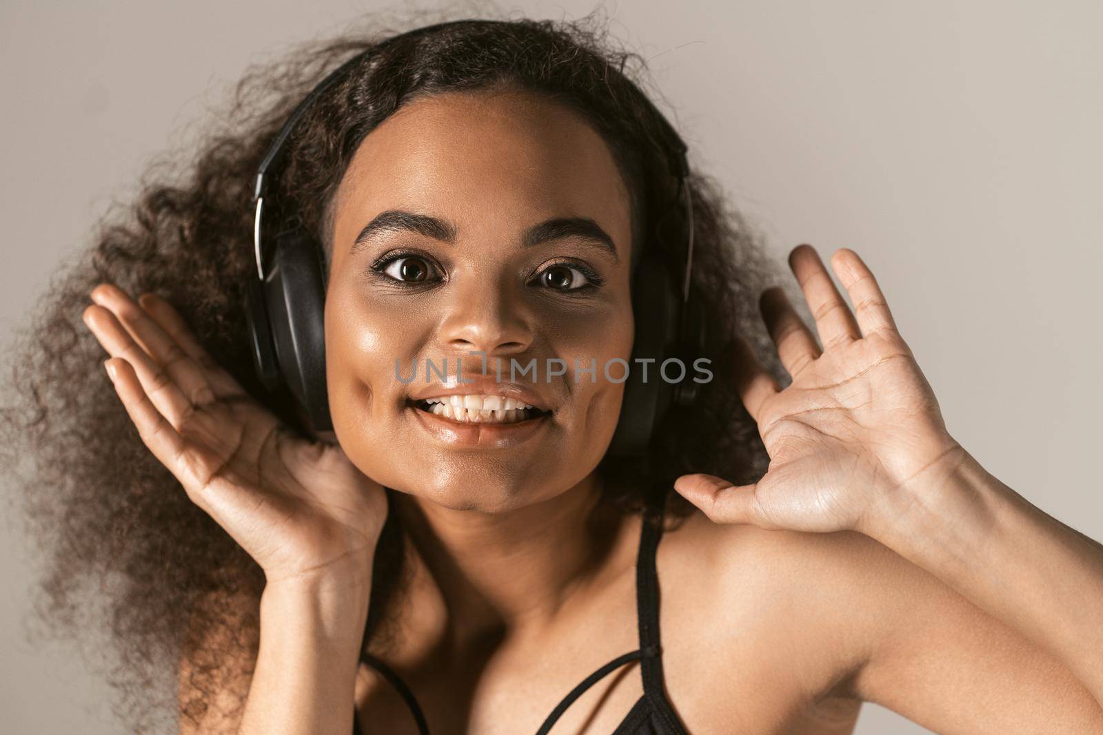 Close up young African-American girl listening music wearing black top in headphones, isolated on grey background, emotionally move, have fun.
