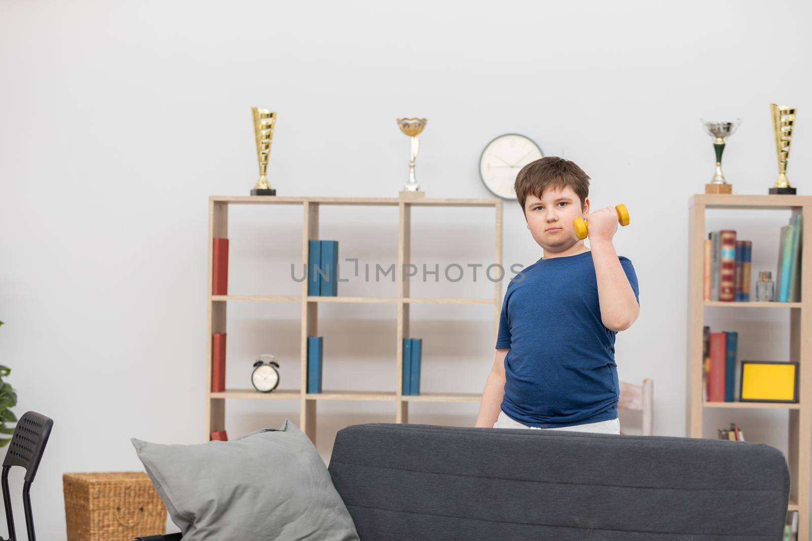 A young boy exercises with dumbbells in his room. by fotodrobik