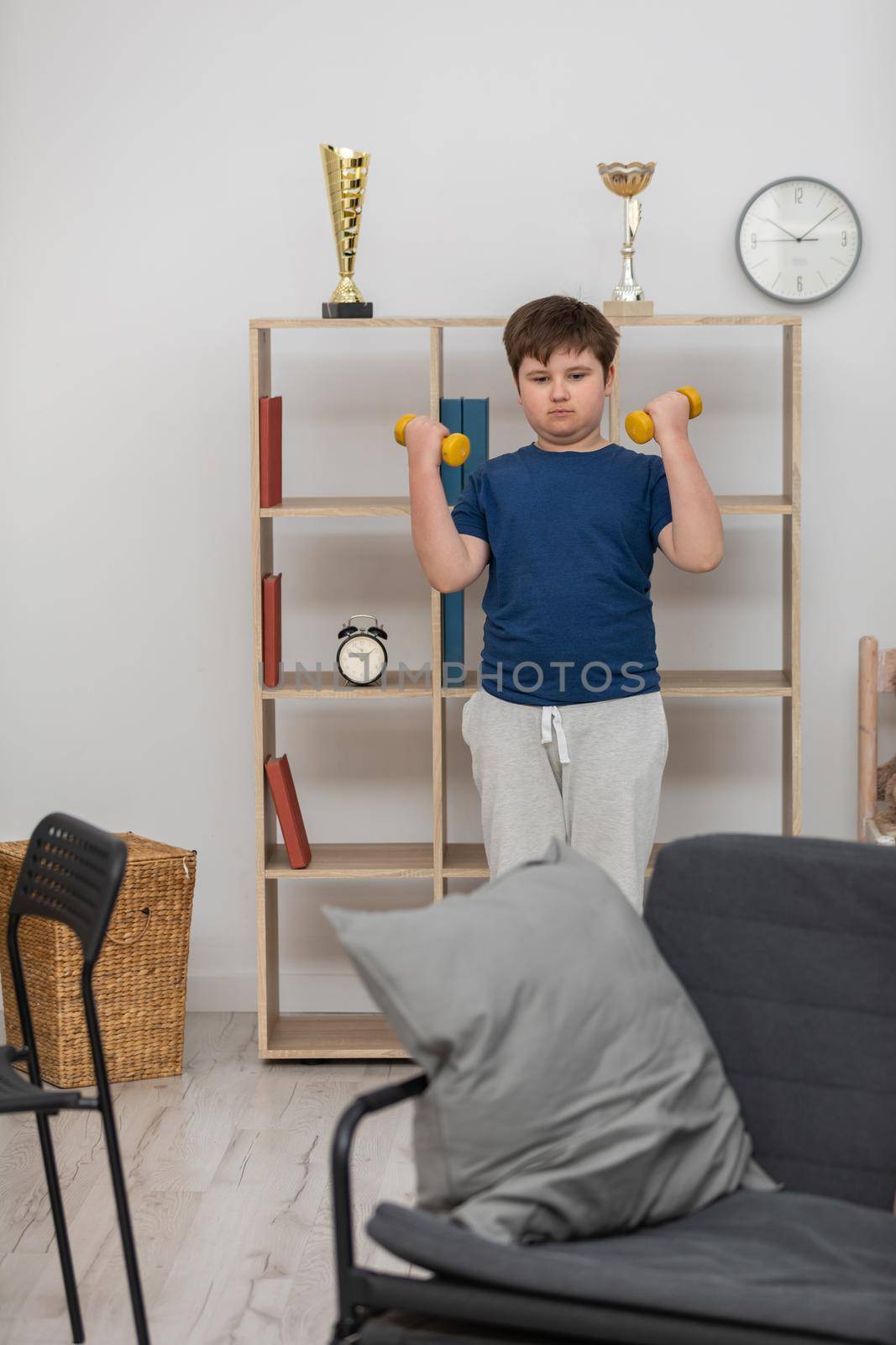 A young boy exercises with dumbbells in his room. by fotodrobik