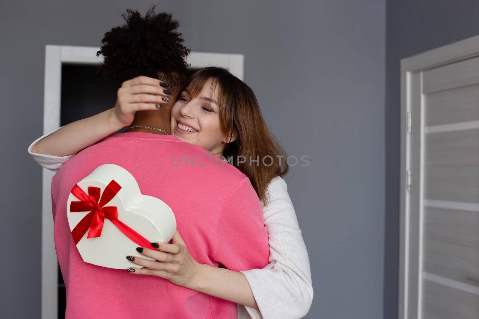 A beautiful girl, hugging her boyfriend , holds a white box in the form of a heart with a bow in her hands by Zakharova