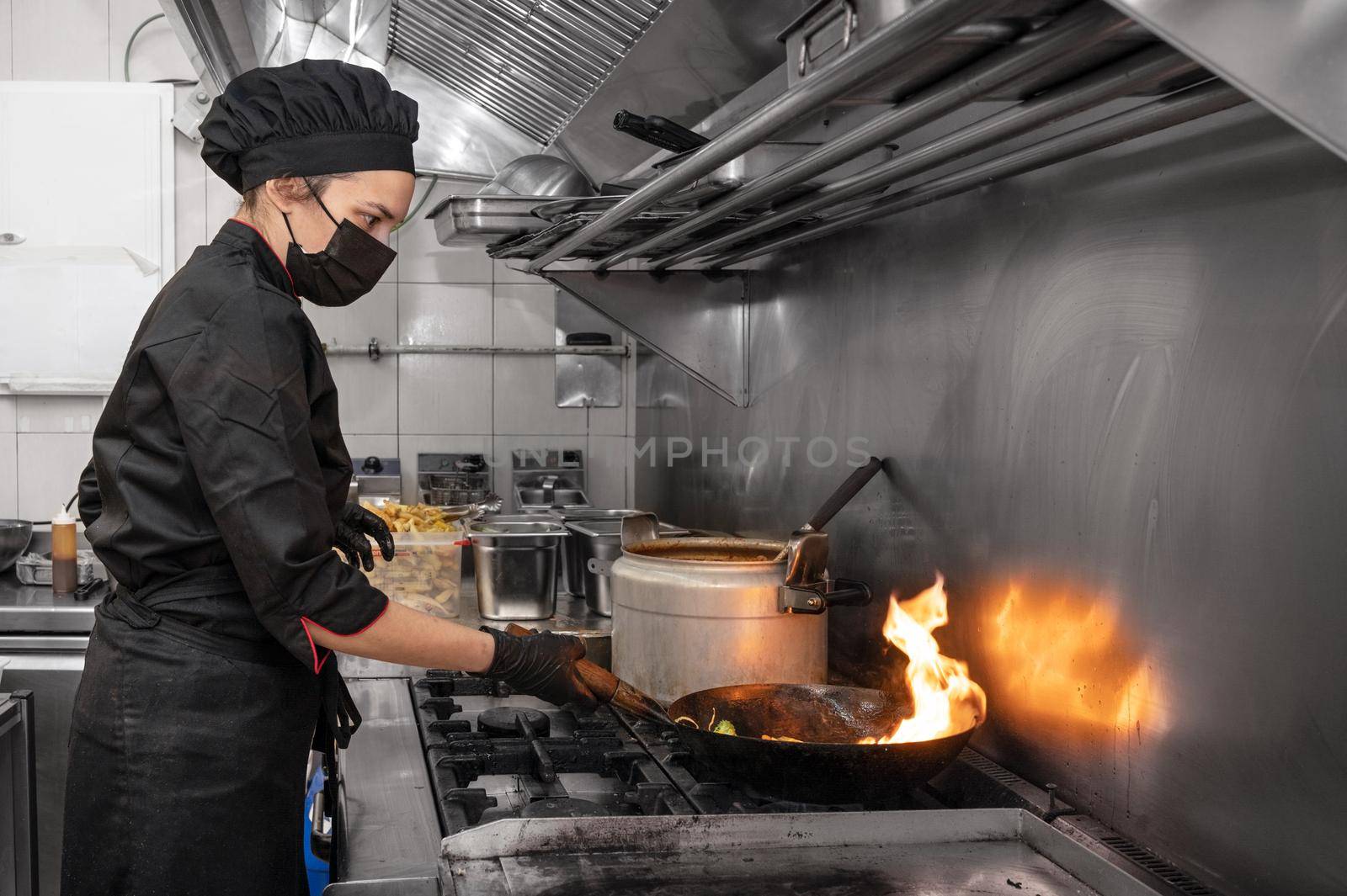 Woman Chef in protective face mask prepare food in the kitchen of a restaurant or hotel during new normal. Coronavirus prevention concept. High quality photo